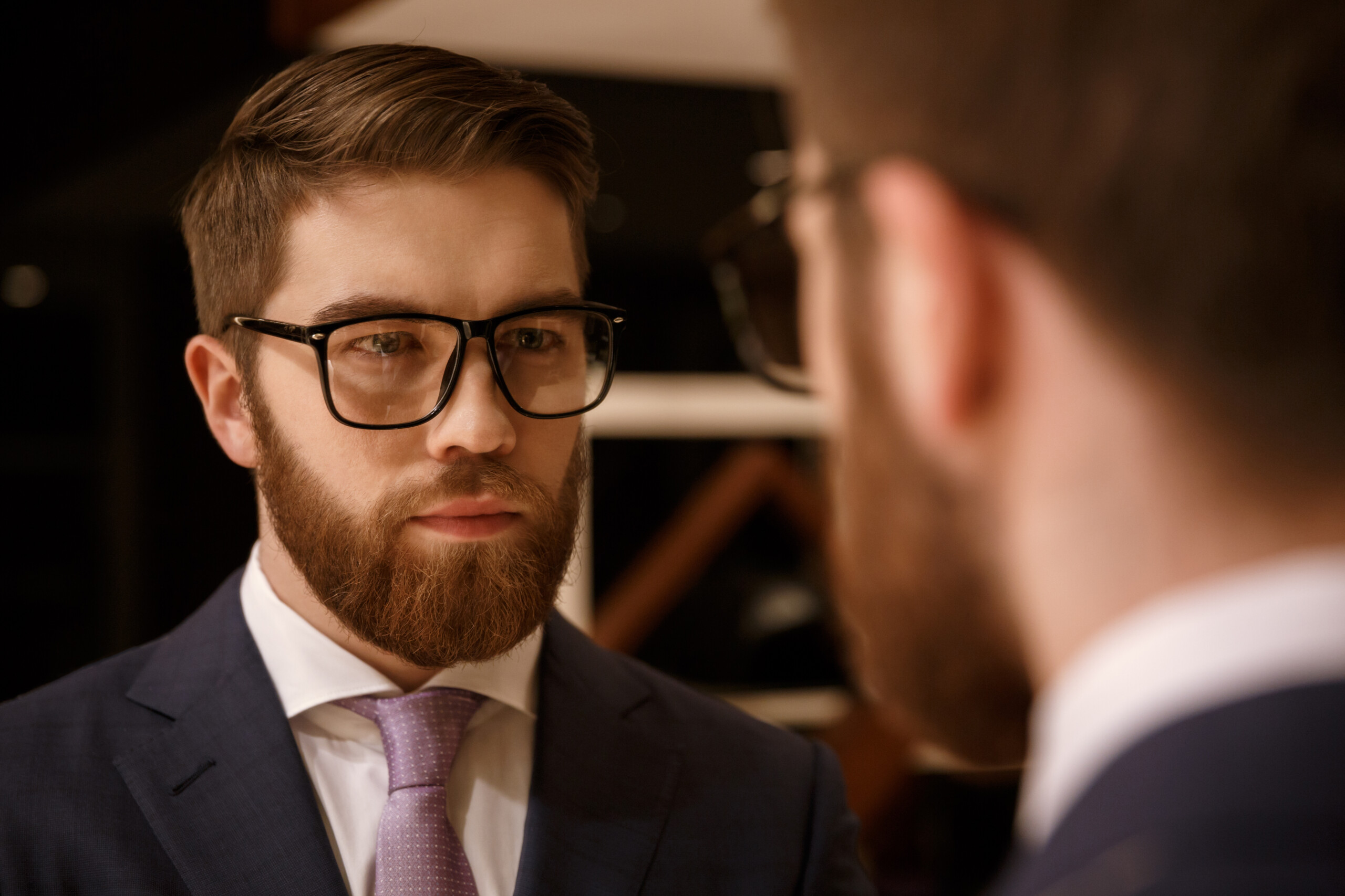 Concentrated young bearded businessman looking at mirror.